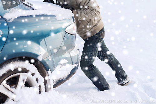 Image of closeup of man pushing car stuck in snow