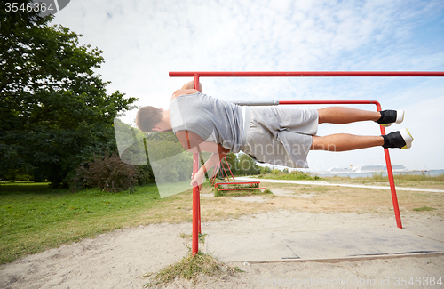 Image of young man exercising on parallel bars outdoors