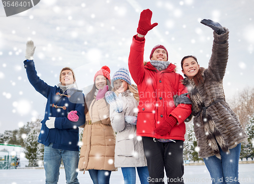 Image of happy friends waving hands on ice rink outdoors