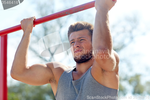 Image of young man exercising on horizontal bar outdoors