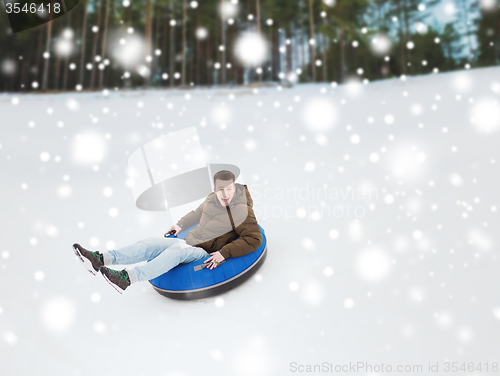 Image of happy young man sliding down on snow tube