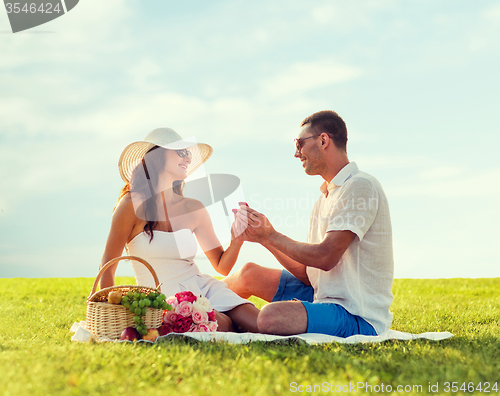 Image of smiling couple with small red gift box on picnic