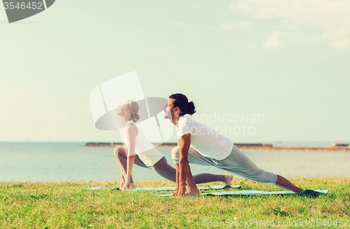 Image of smiling couple making yoga exercises outdoors