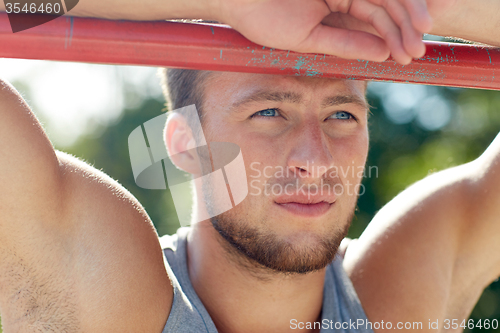 Image of young man exercising on horizontal bar outdoors