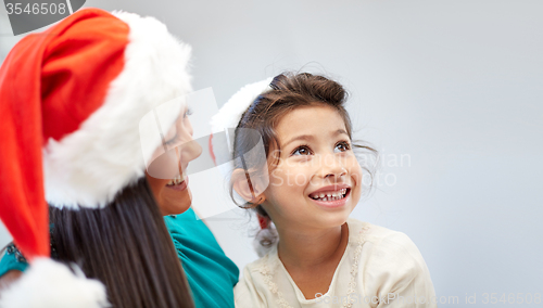 Image of happy mother and little girl in santa hats at home