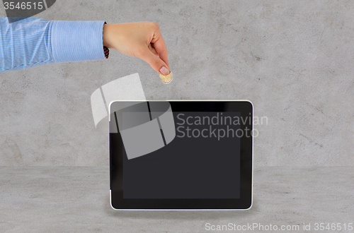 Image of close up of hand putting coin into tablet pc