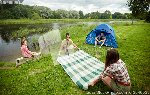 Image of happy friends laying picnic blanket at campsite