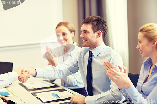 Image of smiling business team shaking hands in office