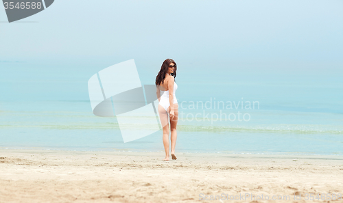 Image of young woman in swimsuit walking on beach