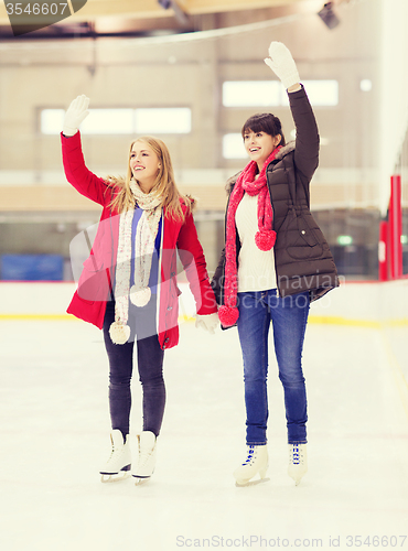 Image of happy girls friends waving hands on skating rink