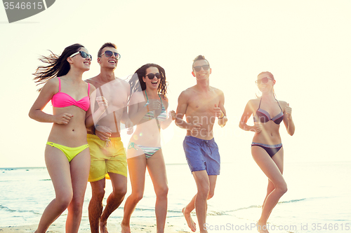 Image of smiling friends in sunglasses running on beach