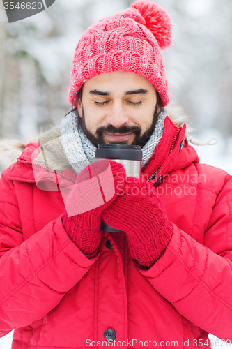 Image of smiling young man with cup in winter forest