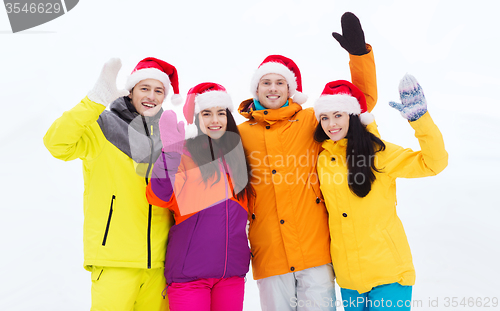 Image of happy friends in santa hats and ski suits outdoors