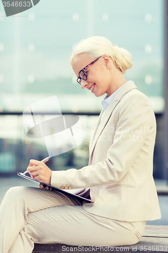 Image of young smiling businesswoman with notepad outdoors