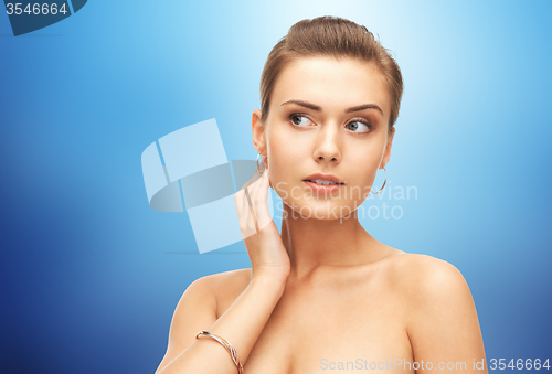 Image of woman with gold earrings and bracelet over blue