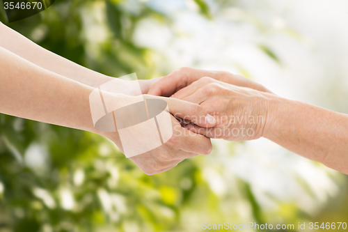 Image of close up of senior and young woman holding hands