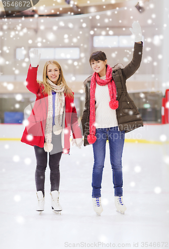 Image of happy girls friends waving hands on skating rink