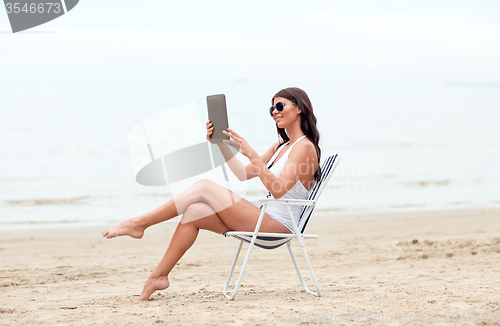 Image of smiling woman with tablet pc sunbathing on beach