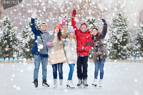 Image of happy friends ice skating on rink outdoors