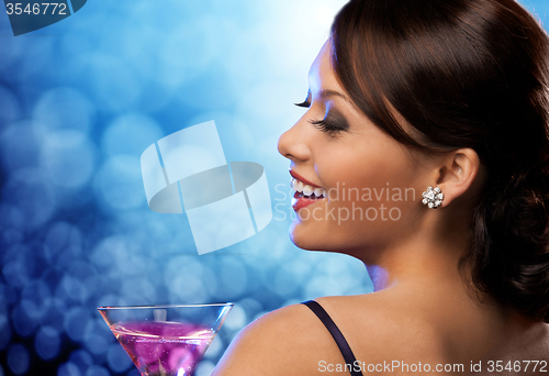 Image of smiling woman holding cocktail over blue lights