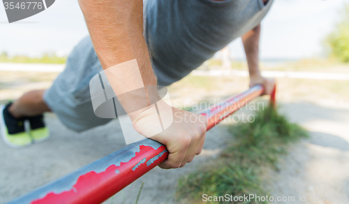 Image of young man exercising on horizontal bar outdoors