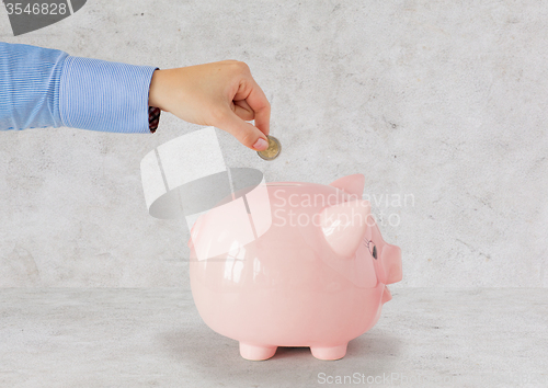 Image of close up of hand putting coin to piggy bank