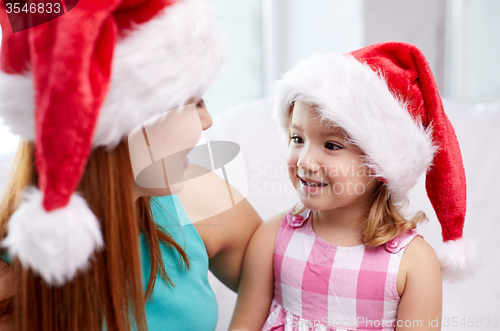 Image of happy mother and little girl in santa hats at home