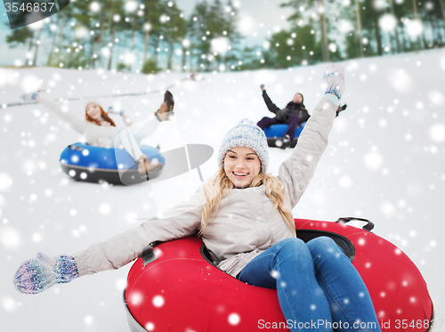 Image of group of happy friends sliding down on snow tubes