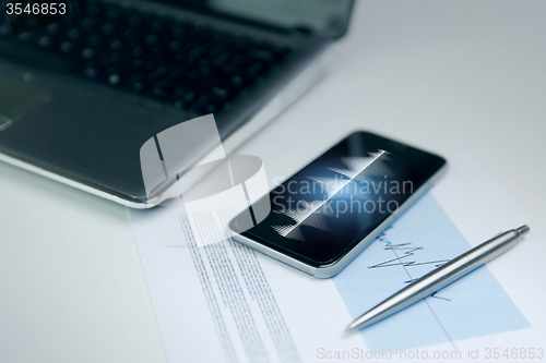 Image of close up of smartphone, laptop and pen on table