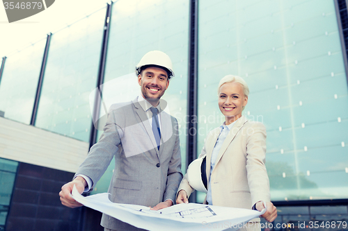 Image of smiling businessmen with blueprint and helmets