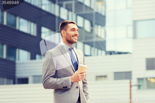 Image of young serious businessman with paper cup outdoors