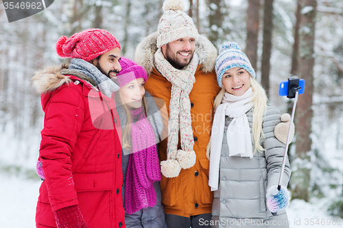 Image of smiling friends with smartphone in winter forest