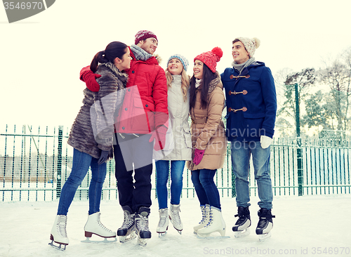 Image of happy friends ice skating on rink outdoors