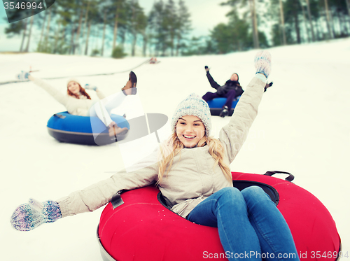 Image of group of happy friends sliding down on snow tubes