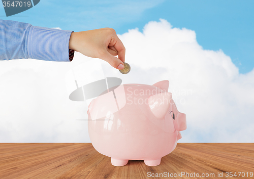 Image of close up of hand putting coin into piggy bank