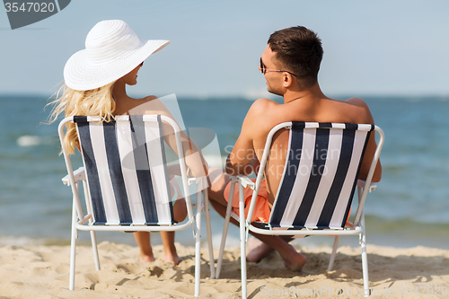 Image of happy couple sunbathing in chairs on summer beach