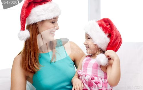 Image of happy mother and little girl in santa hats at home