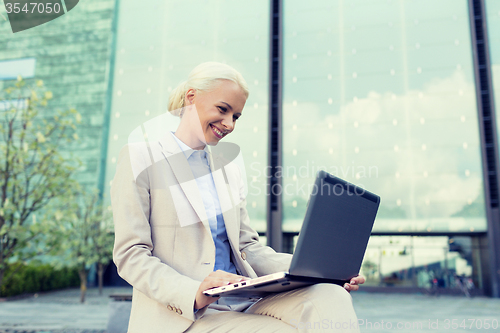 Image of smiling businesswoman working with laptop outdoors