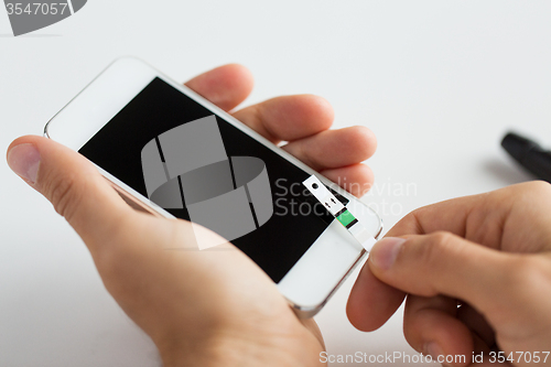 Image of close up of man with smartphone making blood test