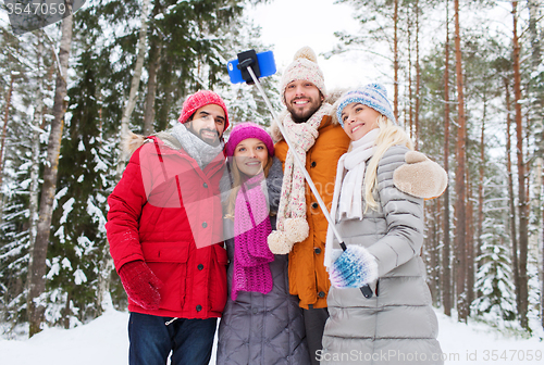 Image of smiling friends with smartphone in winter forest