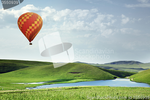 Image of Air balloon flying over the meadows with lake