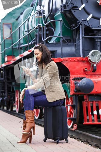 Image of woman sitting on a trunk road and uses the phone