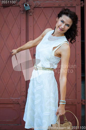 Image of Smiling pretty middle-aged woman in a white dress with a bag