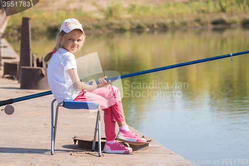 Image of Girl fishing sitting on a chair on the bridge