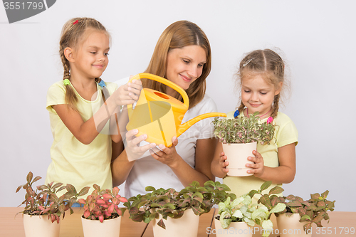 Image of Joyful mother and children watering flowers