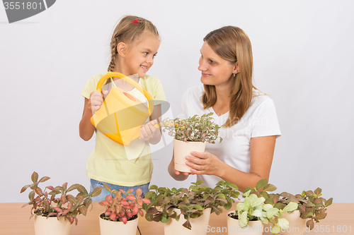 Image of Happy mother and daughter looking at each other watering flowers