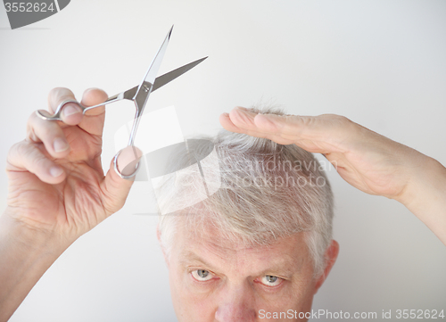 Image of Senior man cuts hair.  