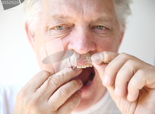 Image of Senior man flosses teeth. 