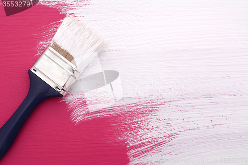Image of Paintbrush with white paint painting over pink