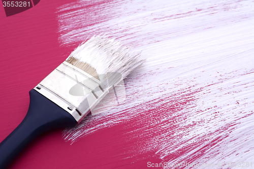 Image of Dirty paintbrush with white paint on half-painted board